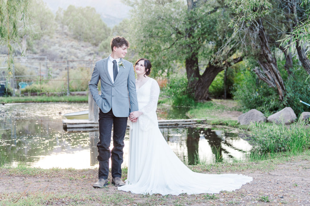 Sunset wedding at New Harmony Utah. Couple in wedding attire standing near a willow pond.